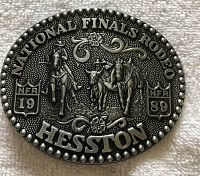 Close-up photo of an oval Hesston branded belt buckle commemorating the 1989 National Finals Rodeo with detailed embossed rodeo scene and text.