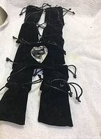 Eleven black velvet-like drawstring pouches arranged on a surface with one glass heart shape placed on top of a pouch to show the contents.