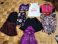 Nine assorted children's clothing items laid on a parquet wood floor.