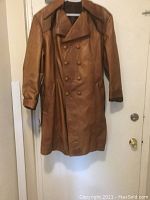 Full view of men's tan leather double-breasted coat with buttons and wide collar, hanging on hanger.