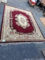 Full view of burgundy rug laid flat on concrete floor showing overall pattern and fringe ends