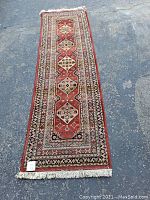 Full length view of the red runner rug laid out on pavement showing overall size and pattern