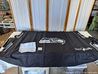 View of black frost guard cover spread out on a table, showing the printed Seattle Seahawks logo and Frost Guard branding, with straps on sides and instructions included.