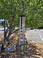 Metal tube chime hanging from a tree with iron chair in background.