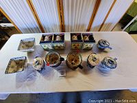 Overview of 12 pieces including 4 boxed mugs, 2 square baking dishes, and 6 lidded ovenware pieces on table.