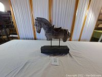 Front view of grey ceramic horse sculpture mounted on black wooden base showing stylized horse torso with carved saddle details