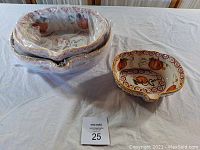 Set of three nesting ceramic bowls covered in plastic wrap on a table, featuring autumn-themed pumpkin designs and scalloped edges.