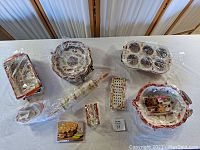 Overview of eight pieces of Temp-tations Autumn Style Old World ovenware still wrapped in plastic on white table.