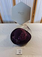 Photo of purple vintage ladies hat with feather and ribbon detail, displayed with Macy's box behind.