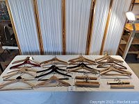 Full view of all wooden coat, jacket, and pant hangers laid out on a table from a top angle. Shows 18 vintage hangers in various wood finishes.