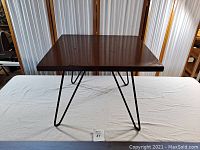 Full view of the square wooden cocktail table top with black metal hairpin legs.