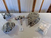 Four vintage Star Wars vehicle models displayed on a white surface: Millennium Falcon, TIE Fighter, X-Wing Fighter, Slave 1, and a clear bag with extra parts.