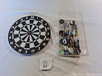 Top view of a 12-inch traditional dartboard with multiple darts in a plastic container beside it showing diverse flight designs.