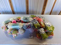 Lot of assorted new rolls of yarn including Caron Simply Soft and Heat Wave brands, multiple colors and pastel shades visible.