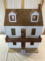 Front view of the vintage wooden doll house showing balcony, windows, and shingled roof.