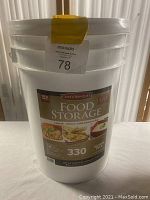 Photo showing large white plastic bucket with label indicating Chef's Banquet Food Storage with 330 servings for one person for one month.