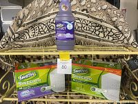 Two boxes of Swiffer Sweeper dry sweeping refills and one bottle of Swiffer WetJet cleaning liquid on display.