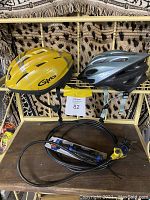Front view of two Giro Icicle helmets, sports air pump, and bicycle lock on a brown table