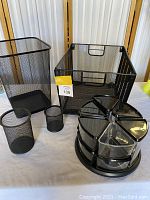 Photo of black mesh office organizers including wastebasket, storage bin, pen holders, and rotating compartment organizer grouped together.