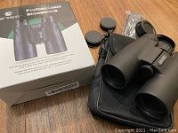 Binoculars placed on carrying case alongside lens caps and sealed accessories, box for identification