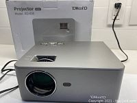 Front and top view of Yoochoo RD-830 mini projector with control buttons visible on top and box in background