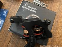 Wormhole coil tattoo machine resting on its box, showing the black frame and red coil wraps, part of tattoo accessories visible nearby.