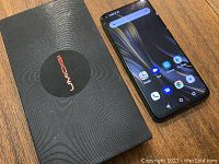 Phone powered on next to UMIDIGI branded box showing open-box contents