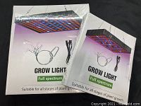 Two shrink-wrapped sealed boxes of full spectrum grow lights with mounting cables and power cords shown on front.