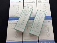 View of 25 infrared thermometer boxes laid out on black surface, showing Kaiyi and Ukeeper branded packaging for non-contact thermometers.