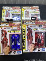 Four Radical Racers remote control cars in original packaging, two red cars and two blue cars, labeled with wall climbing and light-up features