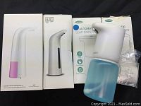 Overview of the three soap dispensers in their boxes with one dispenser and its bottle and accessories outside the boxes