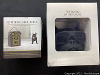 Picture showing boxes of two items: Ultrasonic Bark House and a Bluetooth speaker shaped like a dog with sunglasses.