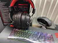 Lot showing RGB backlit gaming keyboard, gaming headphones with red headband, and gaming mouse on plastic container