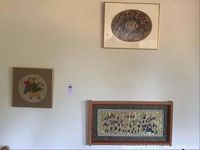 Wall display of two framed embroidered artworks: a circular piece with children and a large rectangular piece with multiple figures and floral patterns.