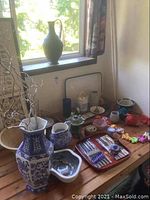 Overview of assortment on wooden table and windowsill, including green ewer, hexagonal vase and assorted items