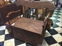 Front-angle view showing carved animal head arms, hinged storage lid, and backrest.