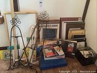 Photo showing easels, sketch and watercolor pads, pastels, artist's mannequin, and art supplies stacked on floor.