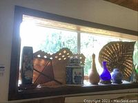 Shelf display of ceramic vases, jars, and woven fans with various decorative patterns and colors including blue-and-white porcelain style.