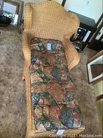 Front perspective of the wicker chaise lounge showing the patterned cushion and design of the arms and backrest.