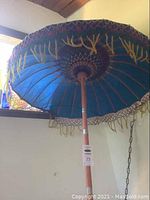 Full view of the tall umbrella showing blue fabric canopy with yellow embroidery and wooden pole.
