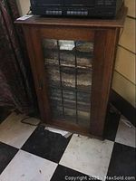 Full view of vintage oak wood cabinet with leaded textured glass door closed sitting on black and white checkered floor.