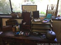 Wide view on wooden surface under window showing teak trinket box, letter holder, stacked wood trays, decorative boxes and framed calligraphy
