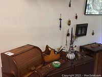 Photo showing wood roll-top bread box, teak wooden holders, two ceramic teapots with blue and white Asian-inspired designs, brass bells, decorative wooden paddle, several wall hanging ornaments.