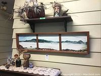Long rectangular wooden framed set of three clay art panels featuring coastal landscape scenes on wall with surrounding decor