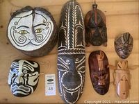 Original painted face and six carved wood masks laid on tabletop, showing different sizes and styles