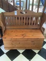 Front view of the wooden storage bench showing the hinged seat and carved backrest with decorative cutouts.
