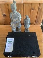 Photo showing two terra cotta soldier figures side by side on wooden table, black box nearby.