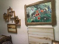 View of three framed original acrylic landscape paintings and wooden wall shelf with figurines on textured wall