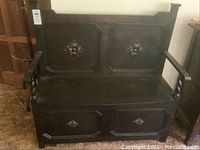 Front view of the dark wood storage bench showing carved floral details on backrest and storage panel below seat, armrests, and overall shape.
