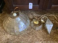Set of three hanging Capiz shell lights on carpet, showing largest dome-shaped, medium round and small faceted pendant shapes, with cords visible including one with Australian plug.